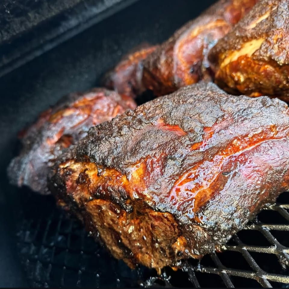 Close-up of several large cuts of barbecued meat with a dark, crispy crust on a grill.