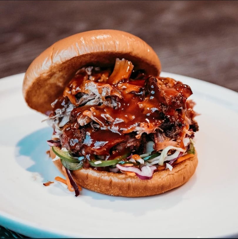 A large pulled pork sandwich with coleslaw and barbecue sauce on a white plate.