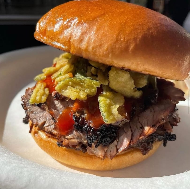 Close-up of a brisket sandwich with BBQ sauce and crispy fried onions on a brioche bun.